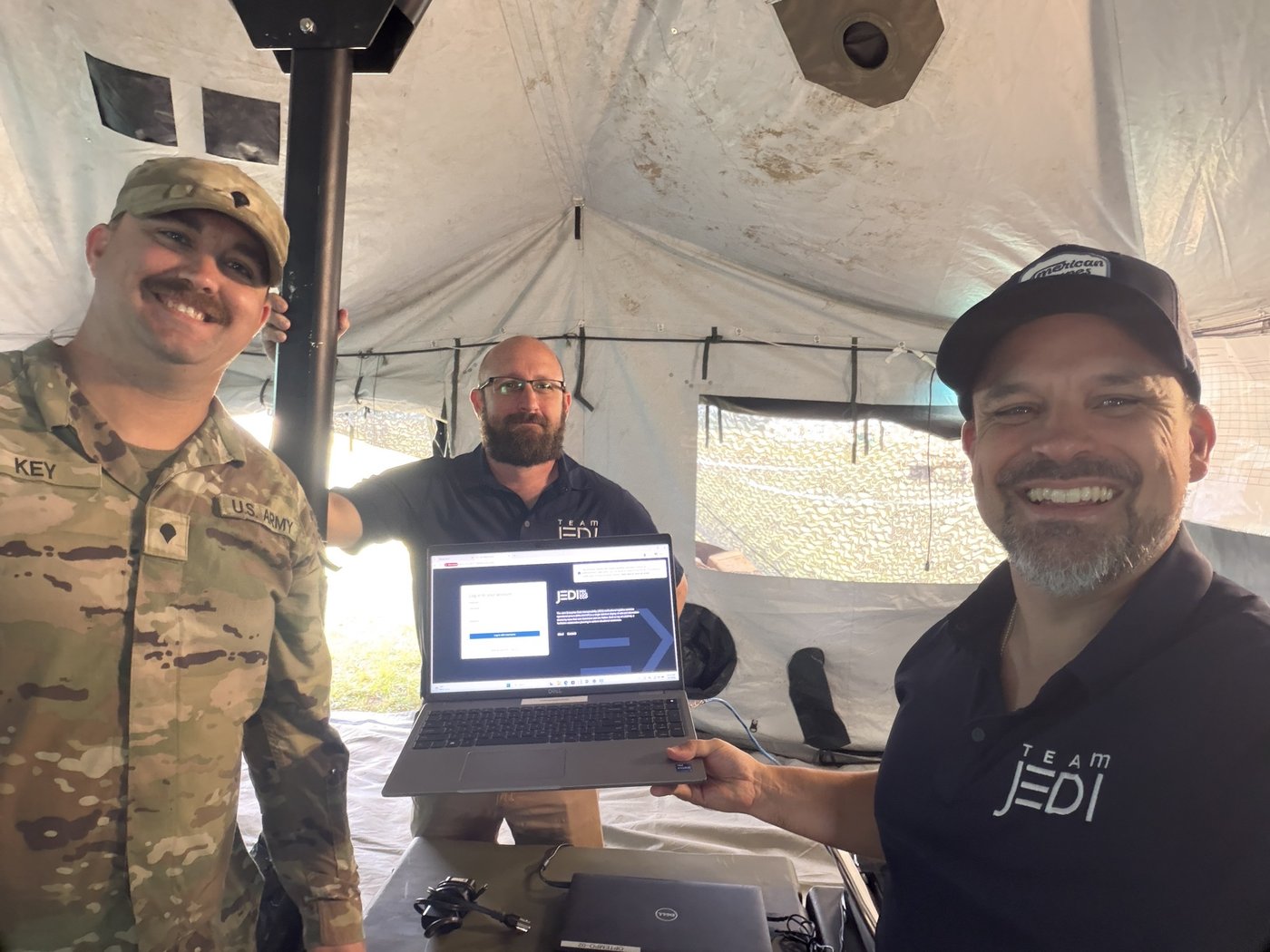 Team JEDI demonstrating JEDI-X on a laptop to a service member inside the field tent
